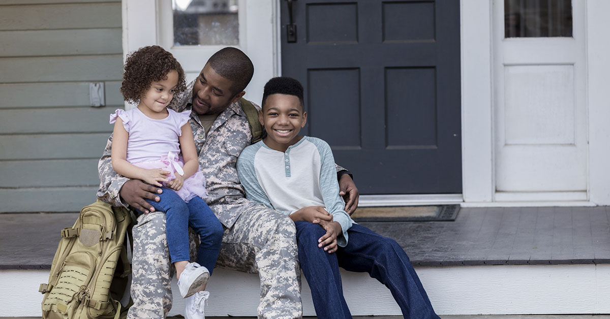 African American Army dad sits on the porch with his preteen son and preschool age daughter before he leaves for an overseas assignment.